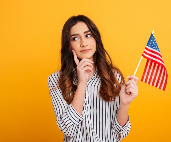 Portrait of a pensive young girl looking away while holding american flag isolated over yellow background